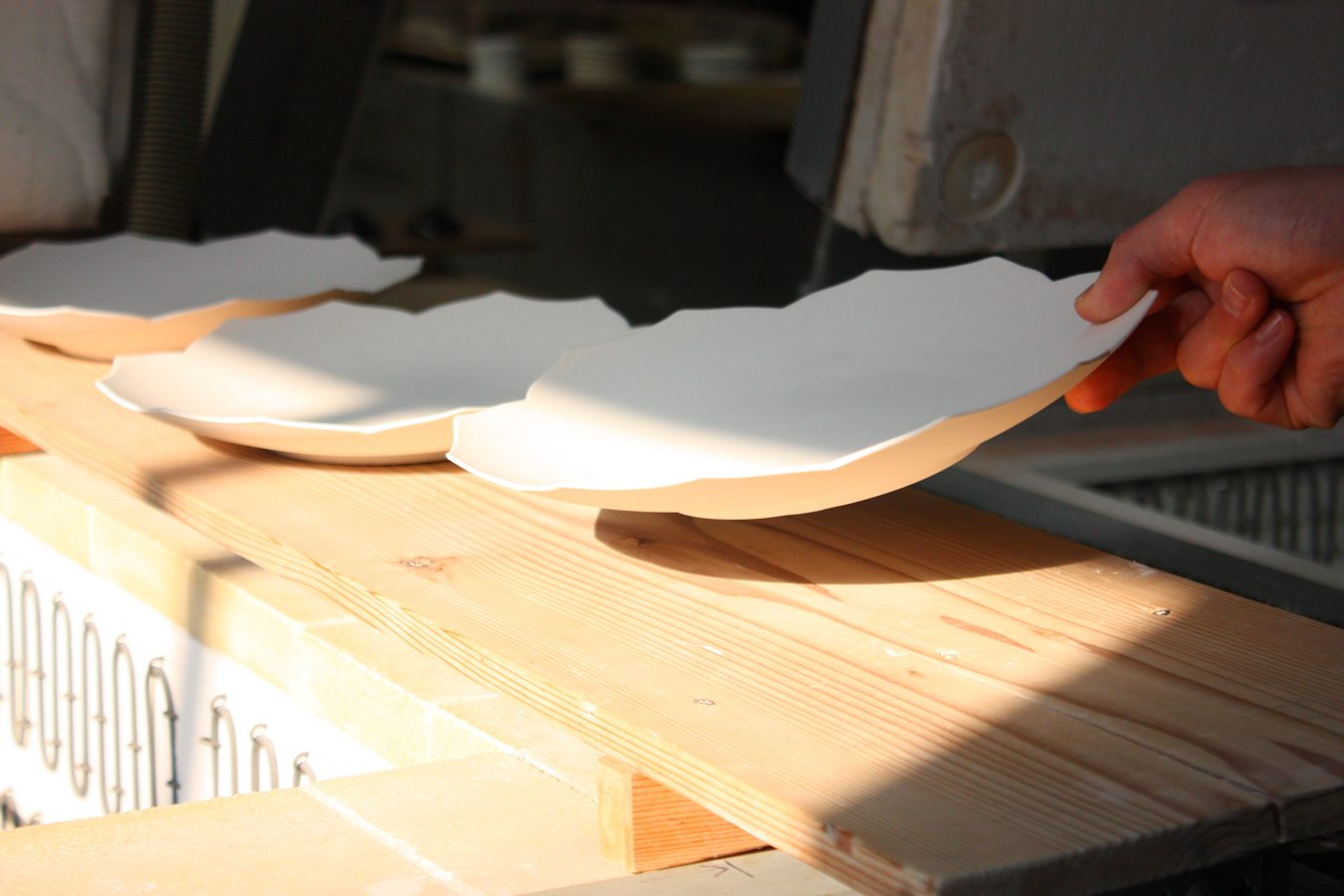 A hand setting a white plate on a board beside the kiln, Touan workshop, Kyoto