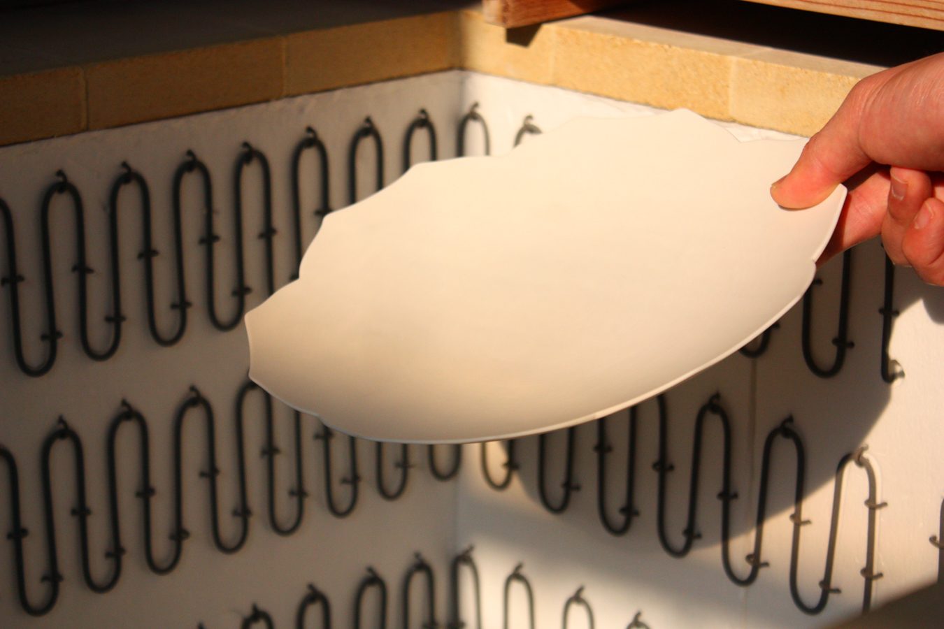 A hand holding a white plate up to the kiln