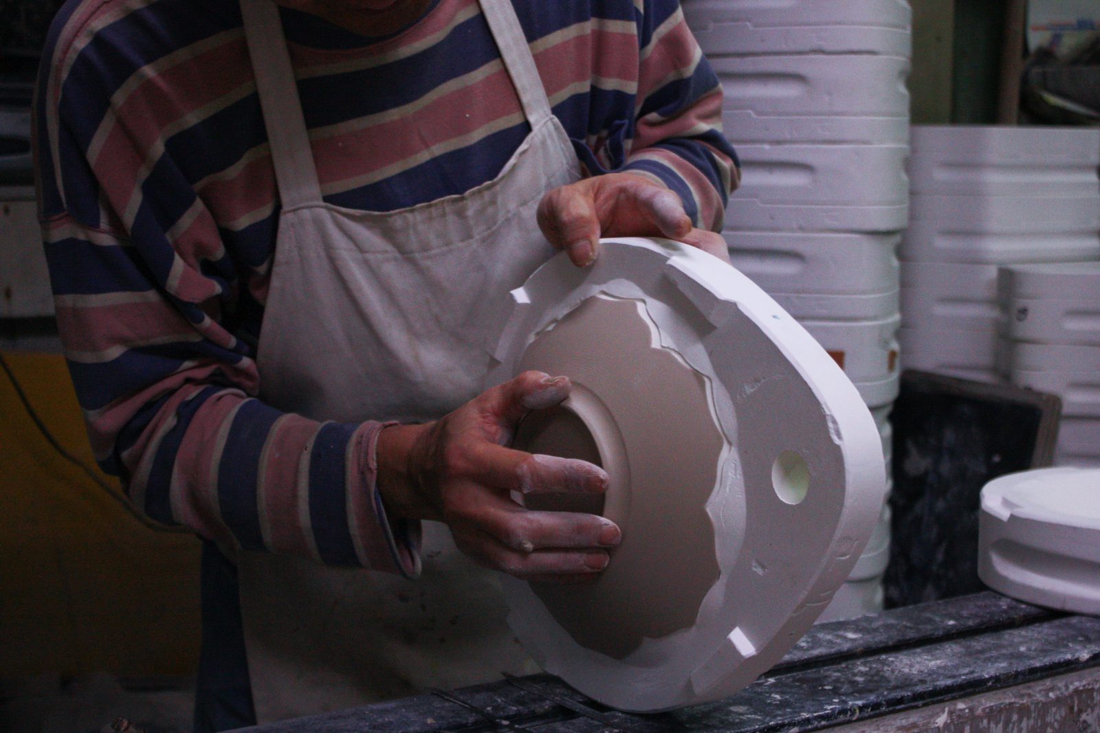 An artisan lifting a plate from its plaster mould